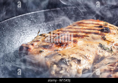 Rauch und Dampf Aufstieg aus einem Schwein Steak auf dem Grill Pfanne Stockfoto