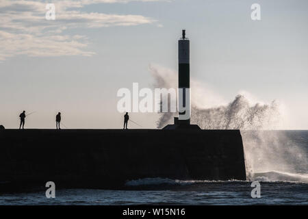 Aberystwyth, Wales, UK. Sonntag, 30. Jun 2019. UK Wetter: Leute angeln in der Nähe des Hafen Leuchtturm in Aberystwyth gespritzt bekommen durch die Wellen auf einer luftigen und kühlen Abend an der Westküste von Wales. Die Temperaturen sind stark von der rekordverdächtigen Höhen der letzten Tage Foto Keith Morris/Alamy Leben Nachrichten gefallen Stockfoto