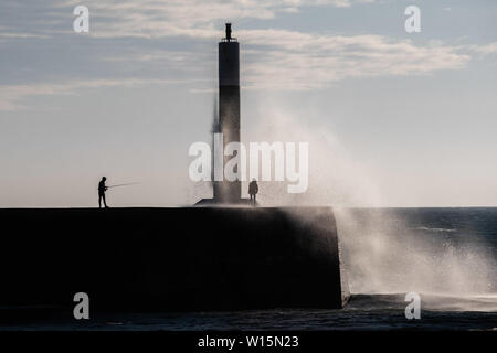 Aberystwyth, Wales, UK. Sonntag, 30. Jun 2019. UK Wetter: Leute angeln in der Nähe des Hafen Leuchtturm in Aberystwyth gespritzt bekommen durch die Wellen auf einer luftigen und kühlen Abend an der Westküste von Wales. Die Temperaturen sind stark von der rekordverdächtigen Höhen der letzten Tage Foto Keith Morris/Alamy Leben Nachrichten gefallen Stockfoto