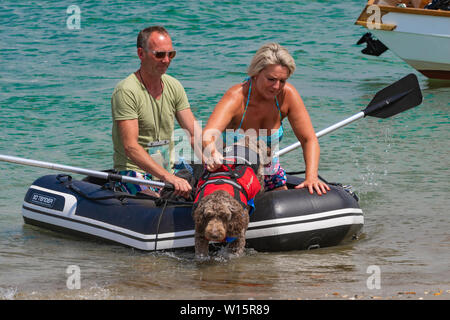 Paar mit Hund in Schwimmweste am Strand in Gummi aufblasbare bei West Wittering, Chichester Harbour, West Sussex, England, Großbritannien Stockfoto