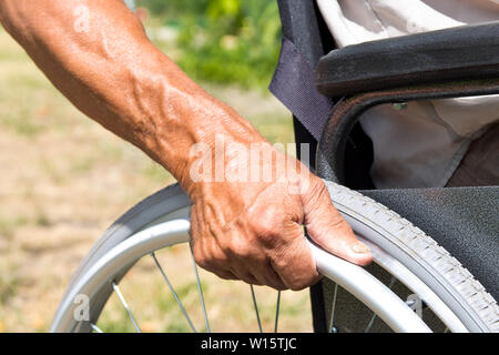 Ein behinderter Mann sitzt im Rollstuhl, hält seine Hände am Lenkrad. Handicap Personen Konzept. Stockfoto