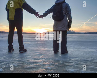 Paar hat Spaß im Winter zu Fuß auf dem Eis der gefrorenen See. Abend Wanderung am Strand von Teich. Warme Kleidung Paar mit hohen warme Stiefel. Stockfoto