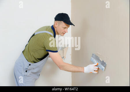 Ein Arbeitnehmer ist Verputzen eine Wand in einer Wohnung mit einem langen Spachtel. Stockfoto