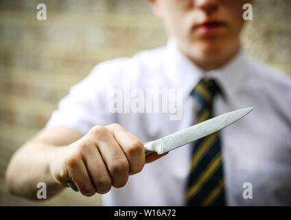 Teenage school boy Holding ein Messer Messer Kriminalität in britischen Schulen zu veranschaulichen Stockfoto