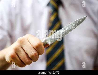 Teenage school boy Holding ein Messer Messer Kriminalität in britischen Schulen zu veranschaulichen Stockfoto