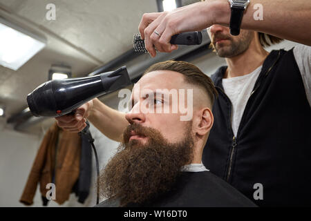 Brutaler Kerl in der modernen Friseur. Friseur Frisur macht ein Mann mit einem langen Bart. Master Friseur nicht Frisur mit Haarschneider Stockfoto