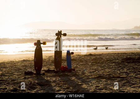 Drei Skateboards aufrecht im Sand am Strand von Pismo Beach, Kalifornien bei Sonnenuntergang, Wellen und Strand Vögel im Hintergrund. Stockfoto