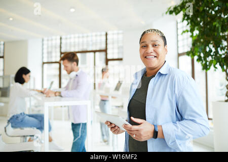 Portrait von Happy neugierige junge Afrikaner - Frau in Männerkleidung stehend an Coworking Space und über mobile App auf Tablet Stockfoto