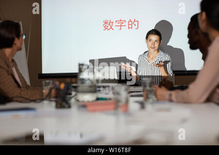Attraktive junge Frau Ausbildung Klasse auf chinesische Kommunikation: Sie zuckte mit den Schultern, während das Erklären, Informationen in der Sitzung Stockfoto