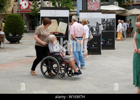 Ältere Frau im Rollstuhl mit einem Hausmeister ihn von hinten in einer Plaza in Granada, Spanien; für einen Spaziergang. Stockfoto