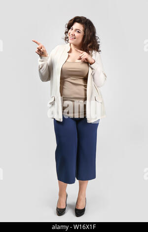 Stilvolle übergewichtige Frau zeigt auf etwas auf hellen Hintergrund Stockfoto