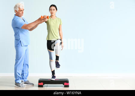 Reifen Physiotherapeuten arbeiten mit jungen asiatischen Frau in Klinik Stockfoto