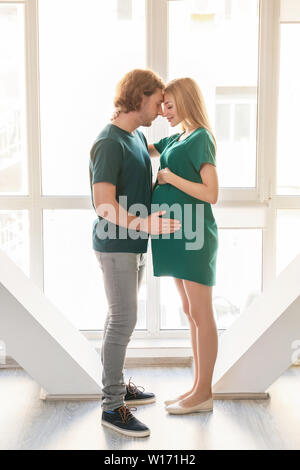 Glückliche junge schwangere Paare in der Nähe der Fenster Stockfoto