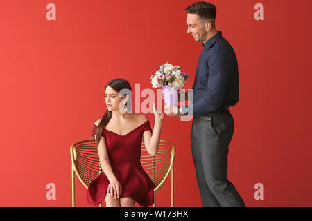 Junge Frau weigert Bouquet von schönen Blumen von Ihrem Freund auf Farbe Hintergrund beleidigt Stockfoto