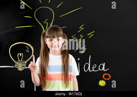 Kleines Mädchen mit erhobenem Zeigefinger in der Nähe von gezeichnet Glühlampen auf dunklen Mauer Stockfoto