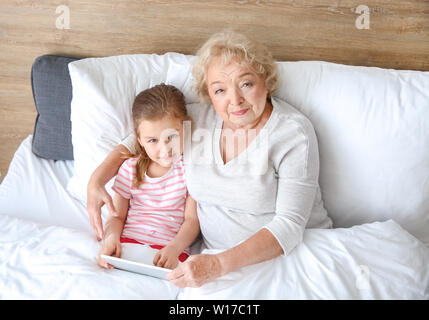 Süße kleine Mädchen mit Großmutter mit Tablet PC im Bett zu Hause Stockfoto