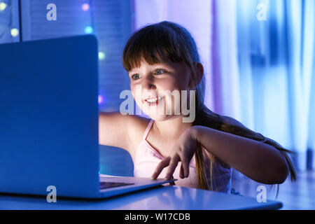 Süße kleine Mädchen mit Laptop am Tisch in der Nacht Stockfoto