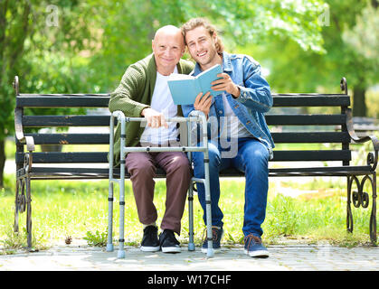 Junger Mann lesen Buch zu seinen alten Vater in Park Stockfoto