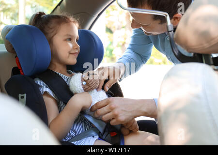 Vater Knickung seine kleine Tochter im Auto Kindersitz Stockfoto