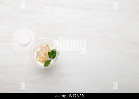 Joghurt birne Schichten und Minze und Pinienkernen liegen in einem Lunch Box auf einem weißen Tisch mit Pinienkernen und Birne Schichten, zerstreut werden. Gesunde Ernährung Konzept Stockfoto