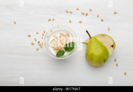 Joghurt birne Schichten und Minze und Pinienkernen liegen in einem Lunch Box auf einem weißen Tisch mit Pinienkernen und Birne Schichten, zerstreut werden. Gesunde Ernährung Konzept Stockfoto