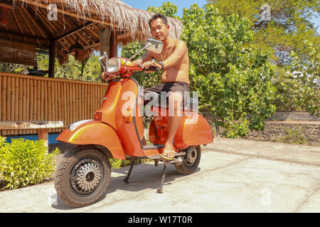 Junge Mann sitzt auf orange Classic Vespa. Orange Classic Vespa. Eine alte orange und schwarz Vespa Super motorscooter ist auf einem Bürgersteig geparkt. Stockfoto