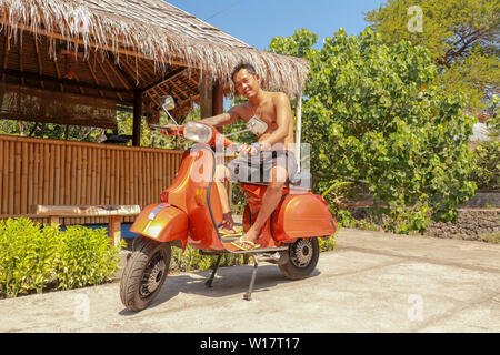 Junge Mann sitzt auf orange Classic Vespa. Orange Classic Vespa. Eine alte orange und schwarz Vespa Super motorscooter ist auf einem Bürgersteig geparkt. Stockfoto