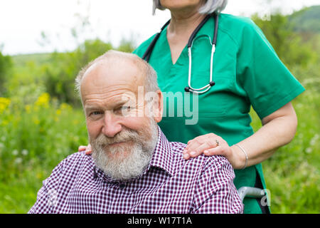 Porträt eines reifen ungültige Mann sitzt im Rollstuhl von freundlichen Krankenschwester outdoor unterstützt. Stockfoto