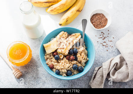 Haferflocken Haferflocken mit Banane, Blaubeere, Nüssen und Honig in blaue Schale auf dem Tisch. Ansicht von oben. Konzept der sauber essen, Gewichtsverlust, Diäten, gesunde lifest Stockfoto