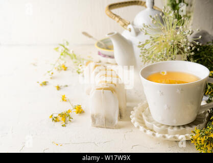 Weißer Tee Tasse mit Teebeutel Kräutertee stehen auf weißen Tisch mit Teekanne und frischen medizinischen Kräuter und Blumen. Close Up. Gesunde vorbeugende Trinken Stockfoto