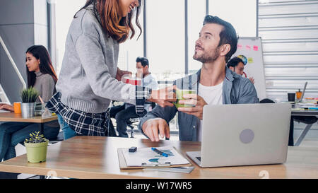 Frau Designer kaufen Kaffeetasse zu Kollegen im modernen Büro in Morgen am Schreibtisch. casual Arbeitsplatz Lebensstil. Stockfoto