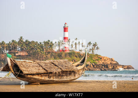 Ein Strand in Kerala, Goa mit einem Leuchtturm im Hintergrund und einem traditionellen Fischerboot im Vordergrund. Stockfoto