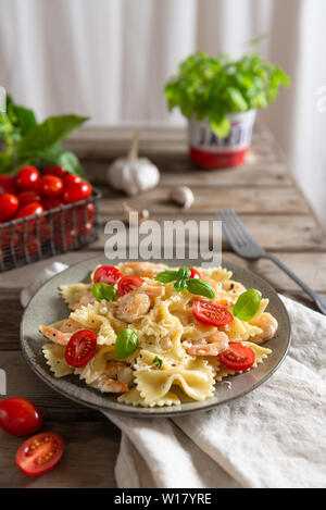 Farfalle und Garnelen mit Knoblauch Sauce, Cherry Tomaten und Basilikum. Italienisches Essen, Küche. Mediterranes Menü. Nahaufnahme Stockfoto