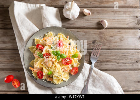 Pasta Farfalle mit Garnelen, Knoblauch, Tomaten und Basilikum Blatt auf Holztisch, italienische Küche, Ansicht von oben. Kopieren Sie Platz für Text Stockfoto