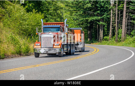 Big Rig leistungsstarke Industrie braun Kipper semi Traktor mit zwei dump Trailer für schwere Lasten, die auf den kurvenreichen Straße in grüne Bäume Wald wi Tuck Stockfoto