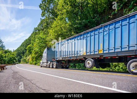 Big Rig grauen mächtigen amerikanischen Motorhaube Long Haul Semi Truck mit verchromten Kühlergrill transportieren riesige überdachte bulk Auflieger bewegen auf dem markierten Weg wi Stockfoto