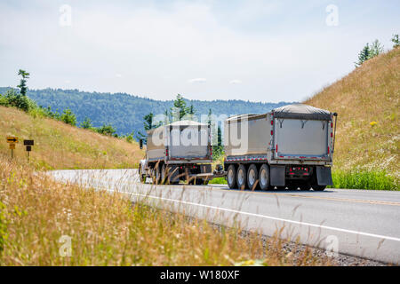 Big Rig leistungsstarke Industrie braun Kipper semi Traktor mit zwei dump Trailer für schwere Lasten, die auf den kurvenreichen Straße in grüne Bäume Wald wi Tuck Stockfoto