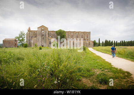 Blick von San Galgano Abbey von außerhalb mit zwei Personen auf dem Weg zur Abtei. Menschen sind nicht erkennbar. Toskana, Italien. Stockfoto