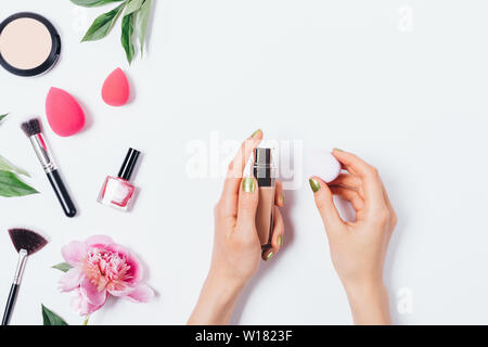 Woman's Hände, die Make-up-blending schwamm Applikator und Gesichtsbehandlung Foundation Cream in der Nähe von Rosa Pfingstrose und feminin Zubehör auf weißem backgroun Stockfoto
