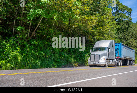 Big Rig grauen mächtigen amerikanischen Motorhaube Long Haul Semi Truck mit verchromten Kühlergrill transportieren riesige überdachte bulk Auflieger bewegen auf dem markierten Weg wi Stockfoto
