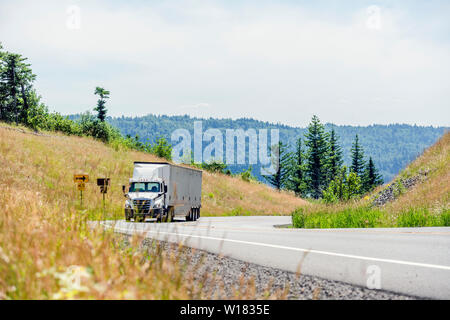 Big Rig White Day Cab Semi Truck mit Dachspoiler transportieren riesige überdachte bulk Auflieger bewegen bergauf auf die kurvenreiche Straße mit gelben h Stockfoto