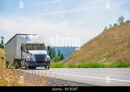 Big Rig White Day Cab Semi Truck mit Dachspoiler transportieren riesige überdachte bulk Auflieger bewegen bergauf auf die kurvenreiche Straße mit gelben g Stockfoto