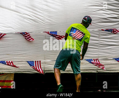 Ein Mann, der ein T-Shirt mit einer amerikanischen Flagge trägt, steht vor einem Wäscheleinen, an dem mehrere kleine amerikanische Flaggen hängen. Stockfoto