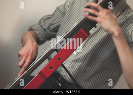 Live Musik im Hintergrund, die Hände eines Mannes spielen Rot moderne elektrische Kontrabass. Nahaufnahme mit selektiven Fokus Stockfoto