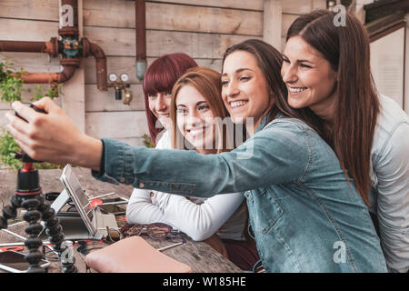 Vier junge vloggers nehmen ein selfie mit einer Kamera lehnte sich gegen ein kleines Stativ im Freien Stockfoto
