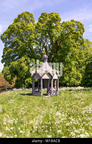 Maytime in den Cotswolds - Zwei weibliche Radfahrer in der 1874 Pumpenhaus vor der schönen alten Bergahorn Baum auf dem Dorfplatz in Farmington UK Stockfoto