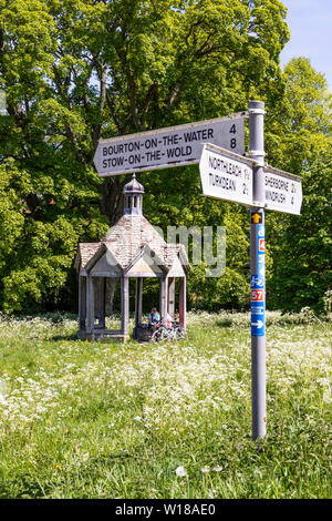 Maytime in den Cotswolds - Zwei weibliche Radfahrer in der 1874 Pumpenhaus vor der schönen alten Bergahorn Baum auf dem Dorfplatz in Farmington UK Stockfoto