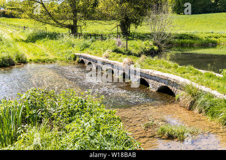 Eine alte Steinbrücke über den Sherborne Bach in der Nähe von Cotswold Village von Sherborne, Gloucestershire, Großbritannien Stockfoto