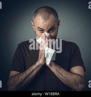 Porträt eines Mannes, der seine Nase weht mit einem Gewebe. Blick in die Kamera. Konzept von Unwohlsein und Allergie. Stockfoto