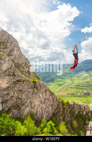 Junge slackliner Mann hängen auf der Slackline betweend zwei Felsen. Highline mit einer schönen natürlichen Landschaft hinter Stockfoto